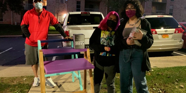 In this photo provided by Jessica Berrellez, her husband, Al Berrellez, left, and daughter Bella Berrellez, right, drop off free desks for Karla Mendez on Tuesday, Sept. 15, 2020, in Gaithersburg, Md.