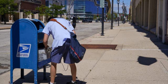 FILE - In this file photo, a U.S. Postal Service worker empties a collection box.
