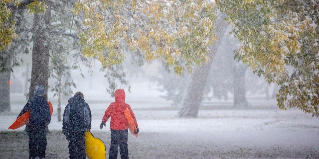 Atticus Saunders, 13, left, Keller Lindstrom, 10, and Fritz Saunders, 11, make their way through the snow after sledding near Lake Nokomis, Tuesday, Oct. 20, 2020, in Minneapolis.