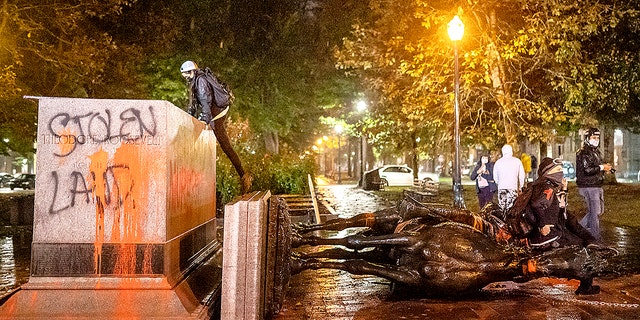 Protesters stand over a toppled statue of President Theodore Roosevelt during an Indigenous Peoples Day of Rage protest on October 11, 2020 in Portland, Oregon. (Photo by Nathan Howard/Getty Images)