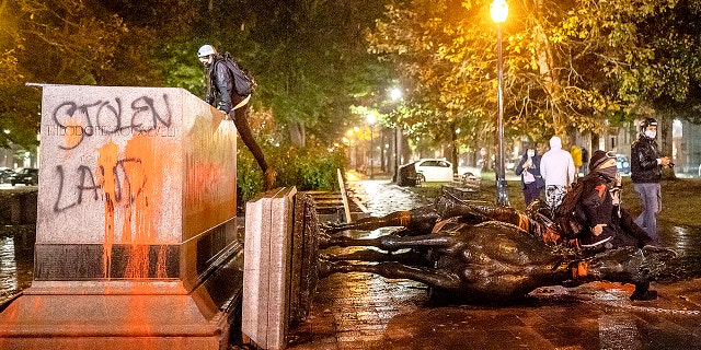 Protesters stand over a toppled statue of President Theodore Roosevelt during an Indigenous Peoples Day of Rage protest on October 11, 2020 in Portland, Oregon. (Photo by Nathan Howard/Getty Images)