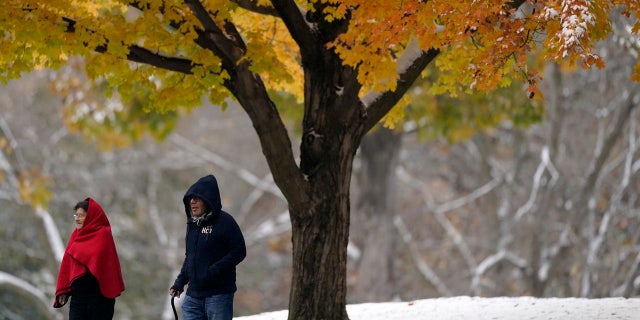 People walk past a glowing tree as they visit a park during the first snow of the season Monday, Oct. 26, 2020, in Merriam, Kan.