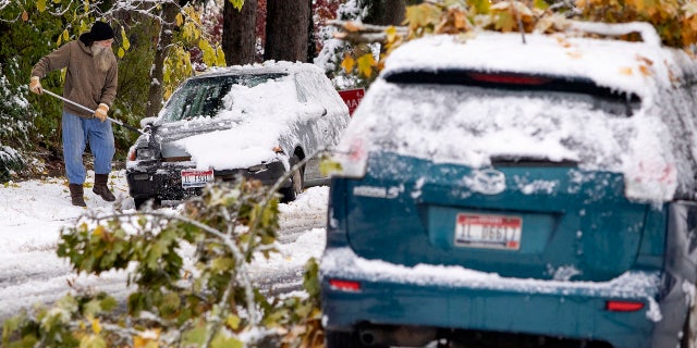 Tim Daulton clears snow off of his car across the street from a car with small tree branches on it on Saturday, Oct. 24, 2020, in Moscow, Idaho.