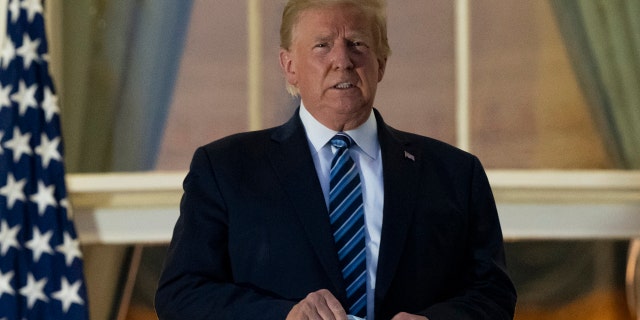 In this Monday, Oct. 5, 2020 file photo, President Donald Trump holds his mask after removing it from his face as he stands on the Blue Room Balcony upon returning to the White House in Washington from the Walter Reed National Military Medical Center in Bethesda, Md. He announced he tested positive for the coronavirus on Oct. 2.