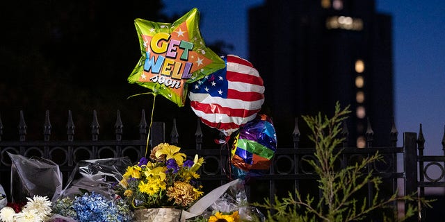 Flowers and balloons left by supporters of President Donald Trump at the entrance to Walter Reed National Military Medical Center (background) in Bethesda, Md., Sunday, Oct. 4, 2020. Trump was admitted to the hospital after contracting the coronavirus. (AP Photo/Cliff Owen)