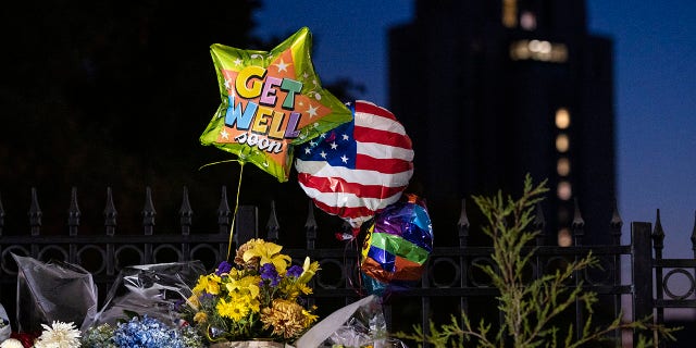 Flowers and balloons left by supporters of President Donald Trump at the entrance to Walter Reed National Military Medical Center (background) in Bethesda, Md., Sunday, Oct. 4, 2020. Trump was admitted to the hospital after contracting the coronavirus. (AP Photo/Cliff Owen)