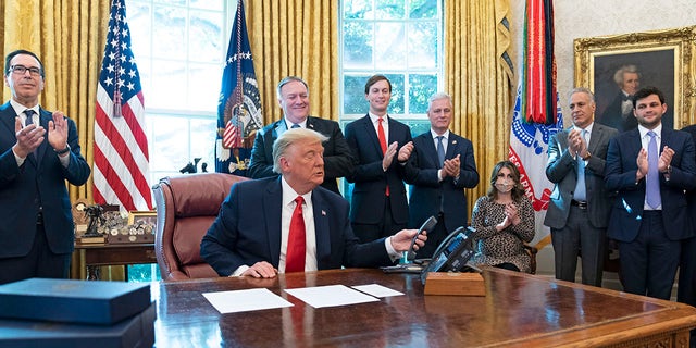 President Trump hangs up a phone call with the leaders of Sudan and Israel, as Treasury Secretary Steven Mnuchin, left, Secretary of State Mike Pompeo, White House senior adviser Jared Kushner, National Security Adviser Robert O'Brien, and others applaud in the Oval Office of the White House, Friday, Oct. 23, 2020, in Washington. (AP Photo/Alex Brandon)