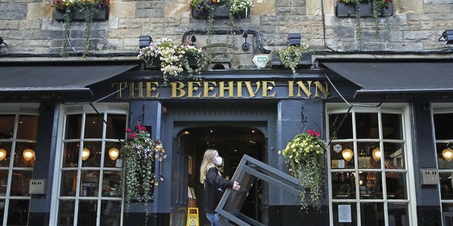 A worker removes tables from outside the Beehive Inn, as temporary restrictions announced by First Minister Nicola Sturgeon to help curb the spread of coronavirus have come into effect at 6 p.m. Friday in Edinburgh. (Andrew Milligan/PA via AP)
