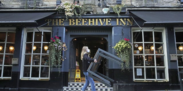A worker removes tables from outside the Beehive Inn, as temporary restrictions announced by First Minister Nicola Sturgeon to help curb the spread of coronavirus have come into effect at 6 p.m. Friday in Edinburgh. (Andrew Milligan/PA via AP)