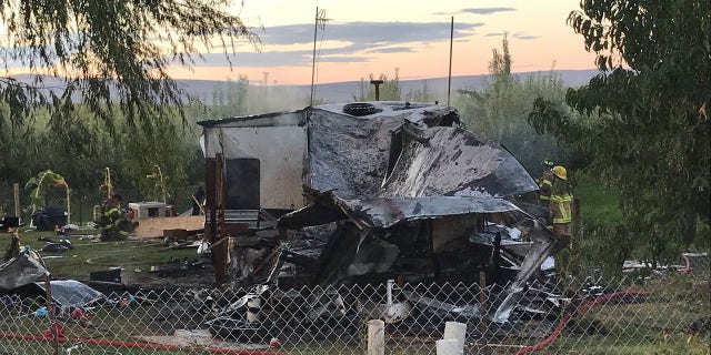 Firefighters examine the charred remnants of the trailer home after it was engulfed in flames early Sunday.