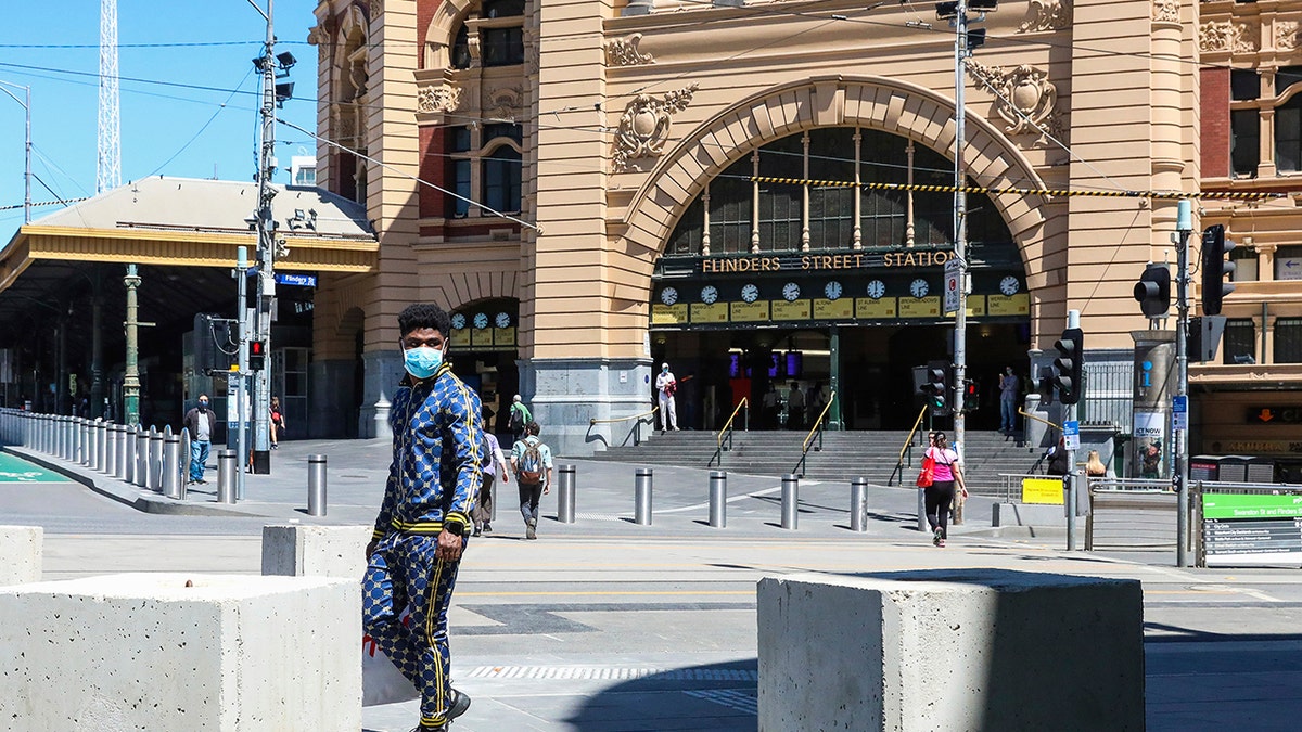A man wearing a mask walks past Flinders Street Station in Melbourne, Australia, Wednesday, Oct. 28, 2020. In Melbourne, Australia's former coronavirus hotspot, restaurants, cafes and bars were allowed to open and outdoor contact sports can resume Wednesday, emerging from a lockdown due to the coronavirus outbreak. (AP Photo/Asanka Brendon Ratnayake)