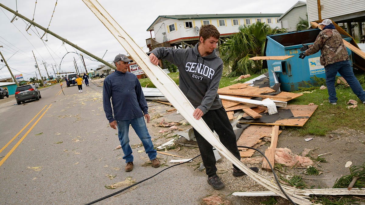 Mark Andollina, left, and his son, Nicholas Andollina, center, remove part of a roof damaged by Hurricane Zeta at the Cajun Tide Beach Resort in Grand Isle, La., Friday, Oct. 30, 2020. (AP Photo/Matthew Hinton)