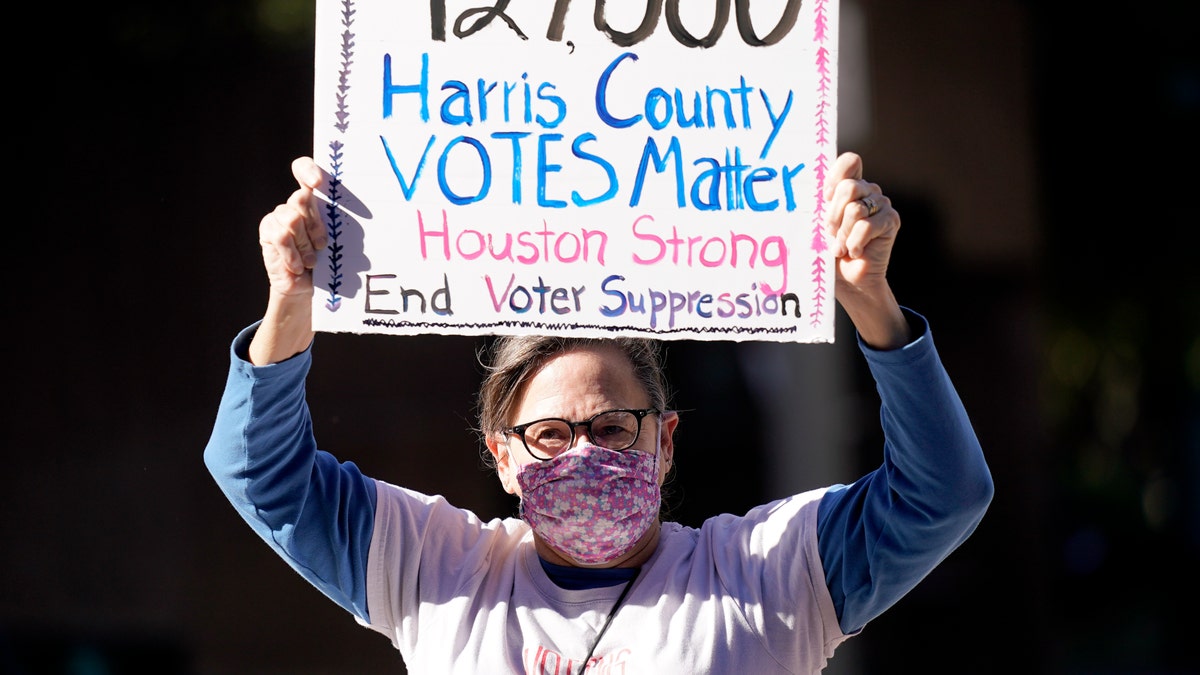 Demonstrator Gina Dusterhoft holds up a sign as she walks to join others standing across the street from the federal courthouse in Houston, Monday, Nov. 2, 2020, before a hearing in federal court involving drive-thru ballots cast in Harris County. (AP Photo/David J. Phillip)