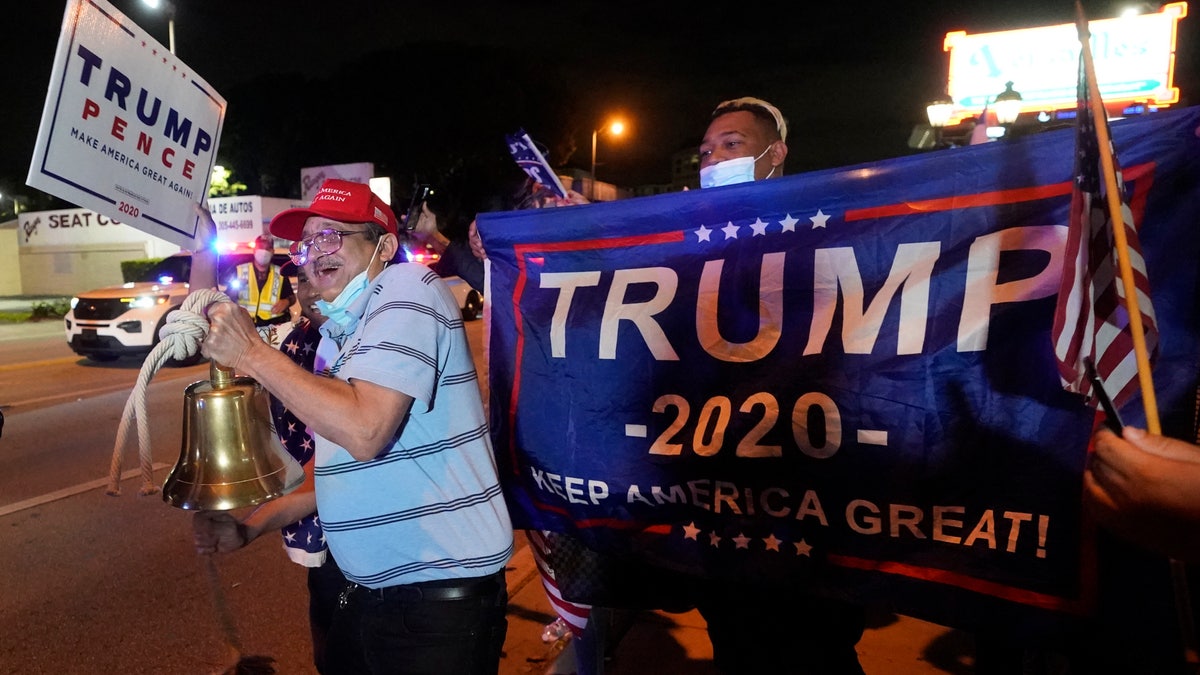 Rafael Fagundo rings a bell as he and other supporters of President Donald Trump chant and wave flags outside the Versailles Cuban restaurant during a celebration on election night, Tuesday, Nov. 3, 2020, in the Little Havana neighborhood of Miami. (AP Photo/Wilfredo Lee)