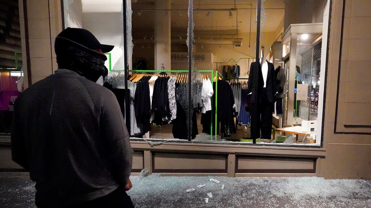 A man stands in front of a broken display window at a retail store during protests in Portland, Ore., Wednesday, Nov. 4, 2020, following Tuesday's election. 