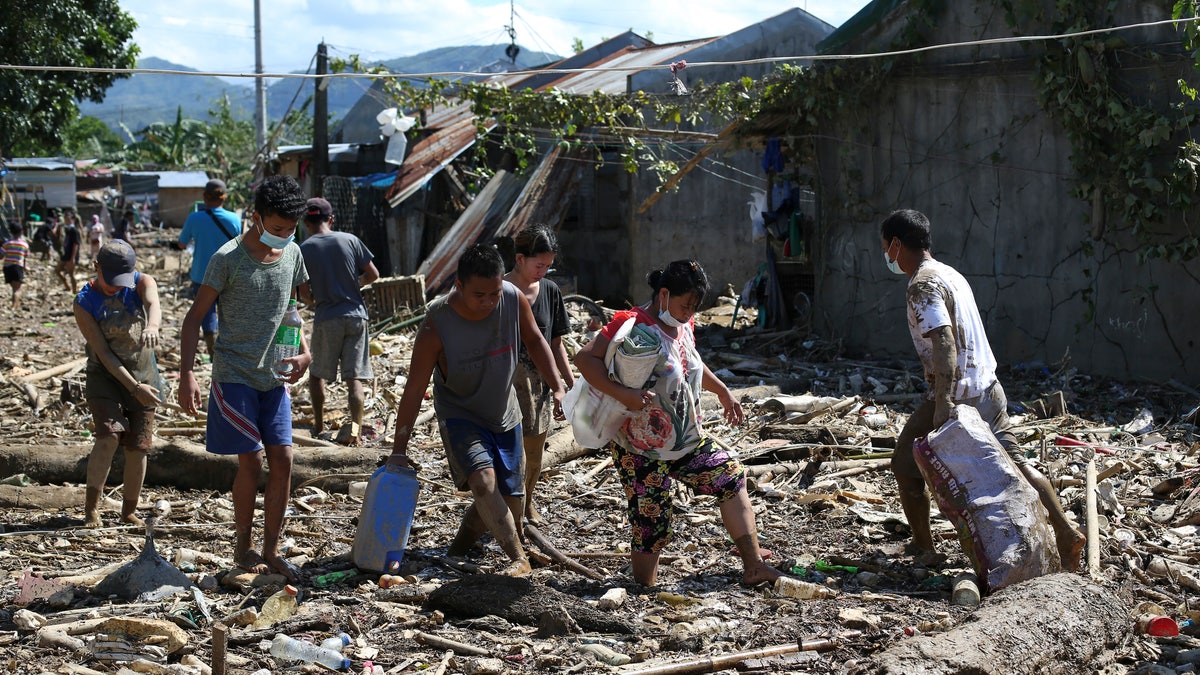 Residents walk through mud and debris at the typhoon-damaged Kasiglahan village in Rodriguez, Rizal province, Philippines on Friday, Nov. 13, 2020. Thick mud and debris coated many villages around the Philippine capital Friday after Typhoon Vamco caused extensive flooding that sent residents fleeing to their roofs and killing dozens of people. (AP Photo/Aaron Favila)