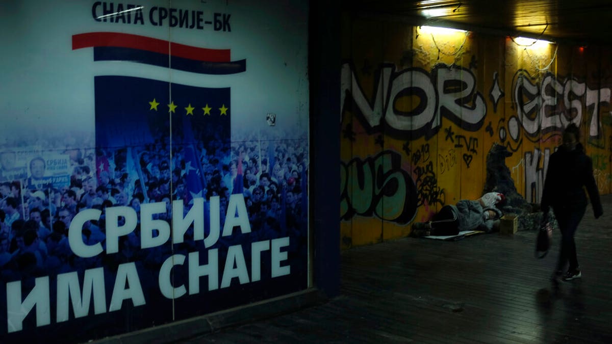 A woman walks through an underground passage by a homeless person and inscription on the wall reading "Serbia has the strength" in Belgrade, Serbia, Monday, Nov. 16, 2020. 