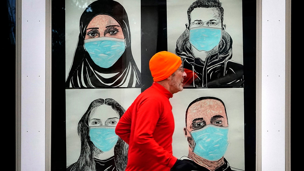 In this Nov. 16, 2020, file photo, a runner passes by a window displaying portraits of people wearing face coverings to help prevent the spread of the coronavirus in Lewiston, Maine. (AP Photo/Robert F. Bukaty, File)