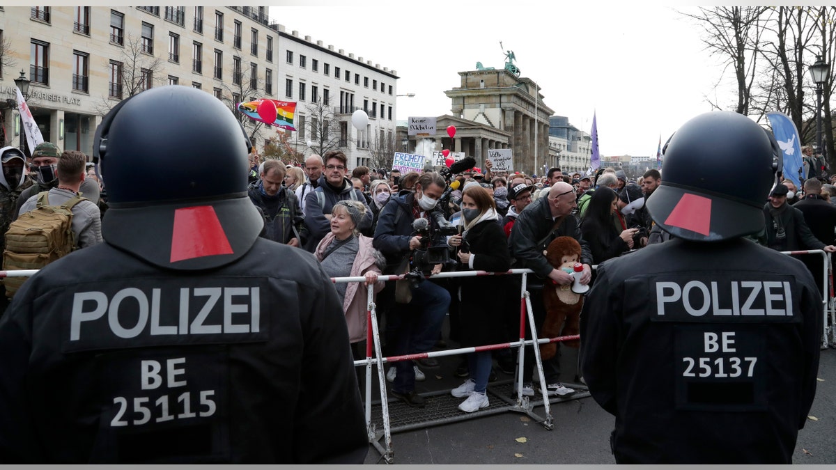 Police officers block a road between the Brandenburg Gate and the Reichstag building, home of the German federal parliament, as people attend a protest rally in front of the Brandenburg Gate in Berlin, Germany, Wednesday, Nov. 18, 2020 against the coronavirus restrictions in Germany. (AP Photo/Michael Sohn)
