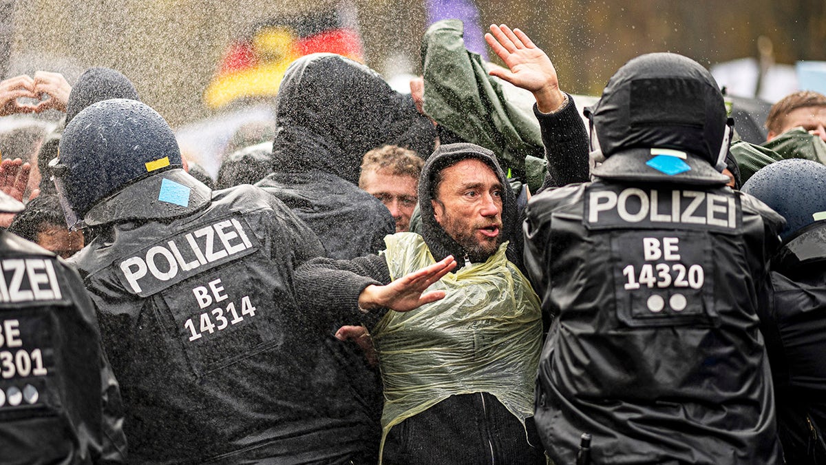 Police officers try to push back protesters on a blocked road between the Brandenburg Gate and the Reichstag building, home of the German federal parliament, as people attend a protest rally in front of the Brandenburg Gate in Berlin, Germany, Wednesday, Nov. 18, 2020 against the coronavirus restrictions in Germany