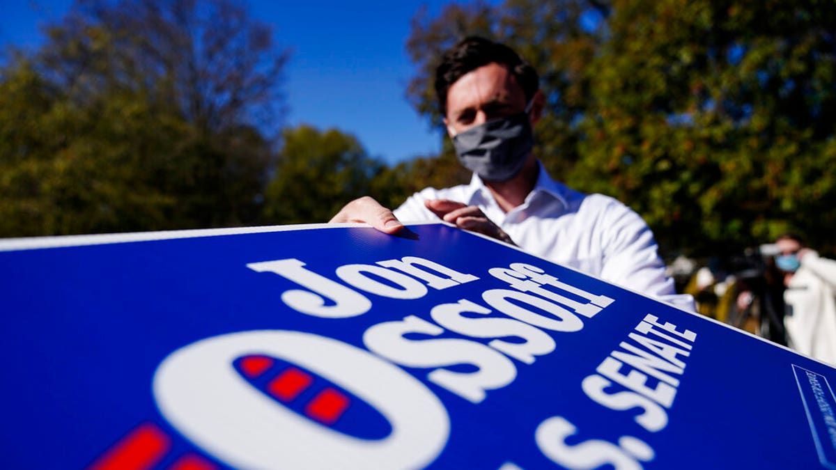 Georgia Democratic candidate for U.S. Senate Jon Ossoff grabs signs to give out during a drive-thru yard sign pick-up event on Wednesday, Nov. 18, 2020, in Marietta, Ga. Ossoff and Republican candidate for Senate Sen. David Perdue are in a runoff election for the Senate seat. (AP Photo/Brynn Anderson)