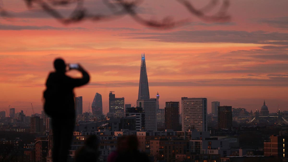 A person takes a photo of the skyline with the Shard building in the center, at sunset, from Greenwich Park in London, Tuesday, Nov. 24, 2020. (Yui Mok/PA via AP)