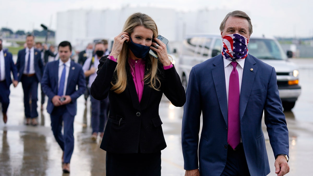 In this July 15, 2020, file photo Sen. Kelly Loeffler, R-Ga., puts on a face mask as she walks with Sen. David Perdue, R-Ga., right, at UPS Hapeville Airport Hub in Atlanta. (AP Photo/Evan Vucci, File)