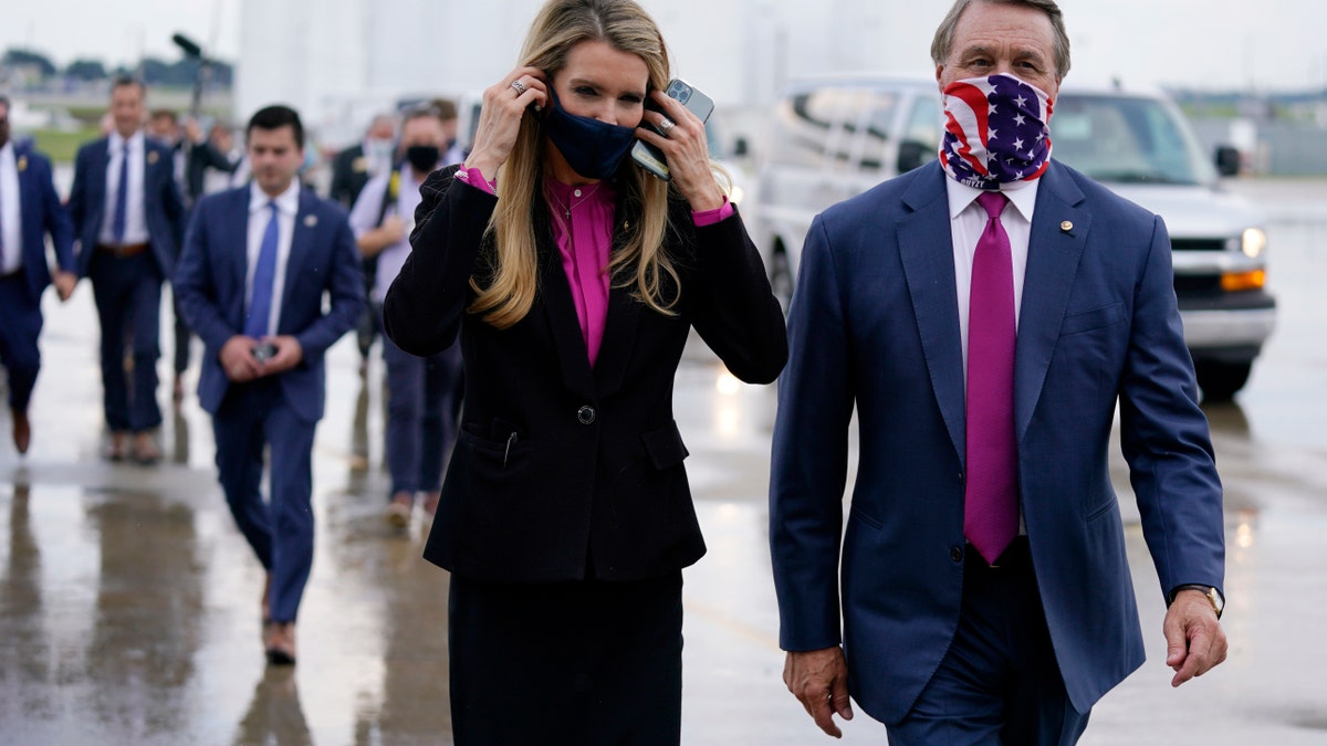 In this July 15, 2020, file photo Sen. Kelly Loeffler, R-Ga., puts on a face mask as she walks with Sen. David Perdue, R-Ga., right, at UPS Hapeville Airport Hub in Atlanta. (AP Photo/Evan Vucci, File)