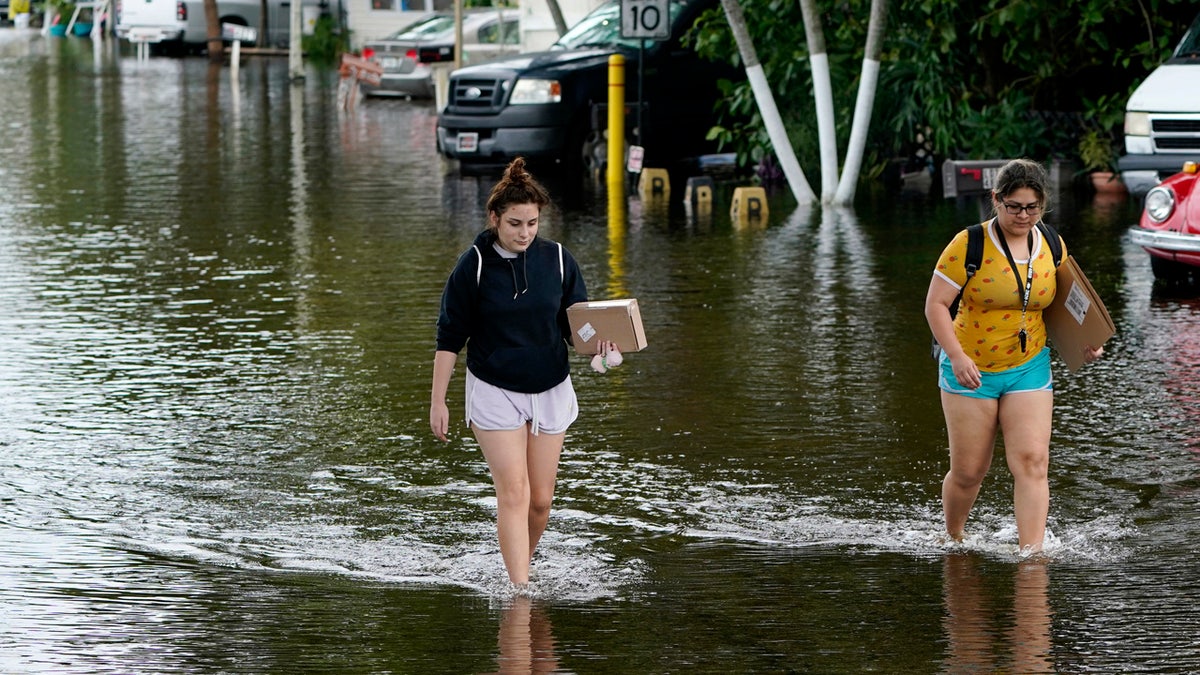 Victoria Rodriguez, left, and Angela Mojica, right, walk on a flooded street in the Driftwood Acres Mobile Home Park, in the aftermath of Tropical Storm Eta, Nov. 10, in Davie, Fla.