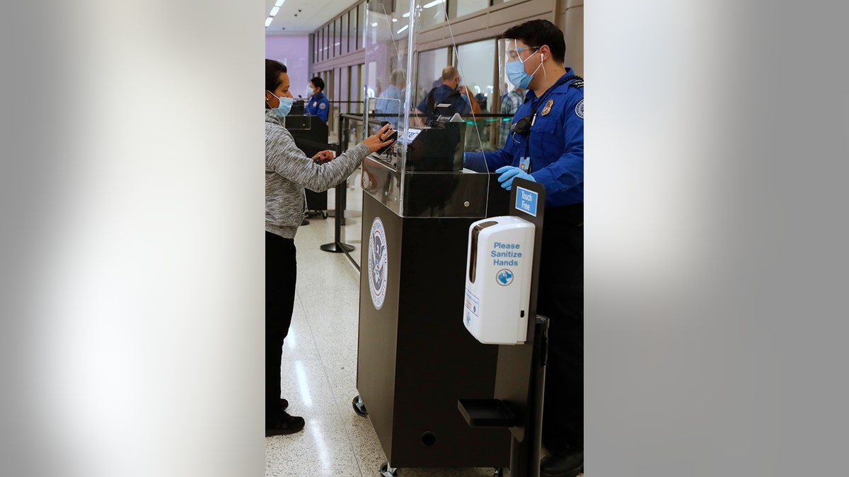 A Transportation Security Administration (TSA) agent wearing a protective face mask and shield checks the identification of a travelers Photographer: George Frey/Bloomberg via Getty Images