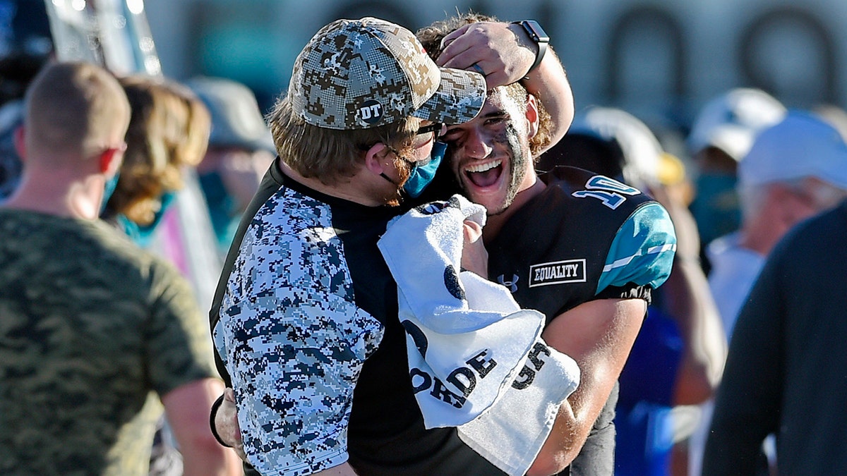 Coastal Carolina quarterback Grayson McCall (10) is hugged by a member of the coaching staff during the second half of an NCAA college football game against Appalachian State, Saturday, Nov. 21, 2020, in Conway, S.C. Coastal Carolina won 34-23. (AP Photo/Richard Shiro)
