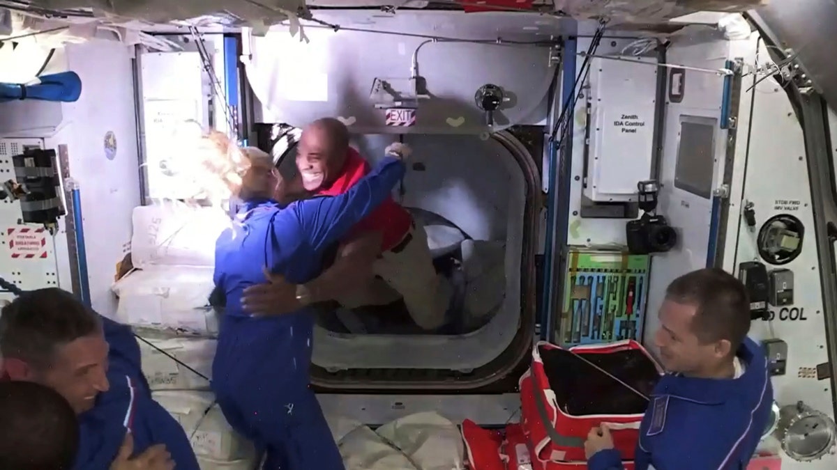 In this frame grab from NASA TV, astronaut Victor Glover, center, is greeted by astronaut Kate Rubins as he enters the International Space Station from the vestibule between the SpaceX Dragon capsule and the ISS, early Tuesday, Nov. 17, 2020. At right is Expedition 64 commander Sergey Ryzhikov. (NASA TV via AP)