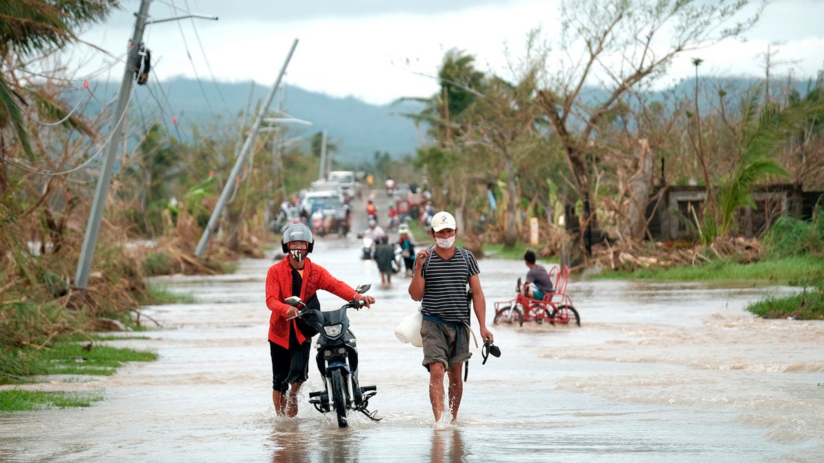 Residents walk past toppled electric posts along a flooded road in Albay province, central Philippines, due to Typhoon Vamco on Thursday, Nov. 12, 2020.