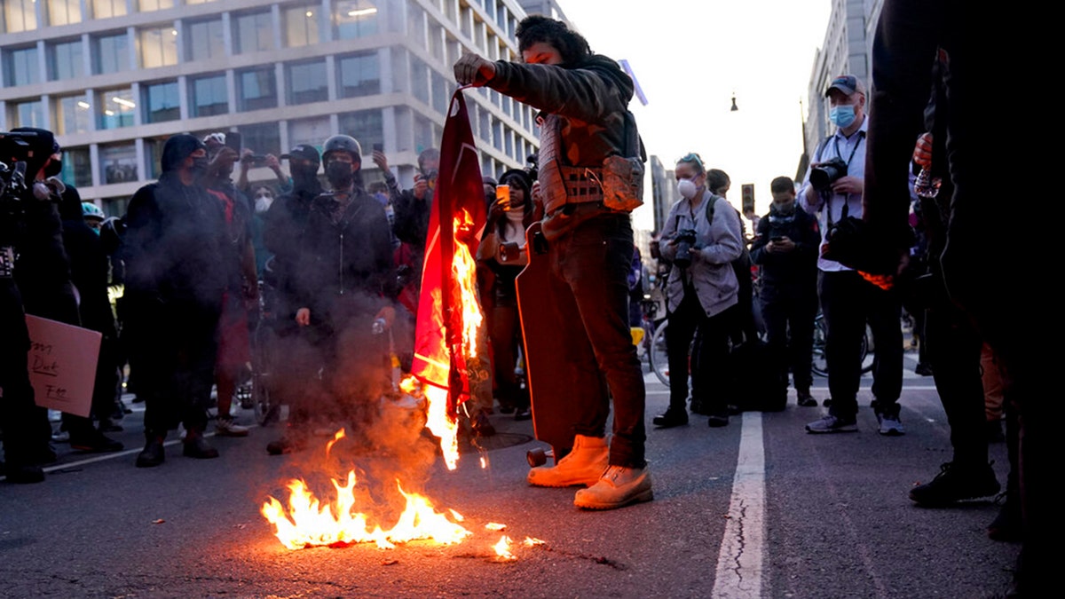 A counter-protester burns a Trump 2020 flag after supporters of President Trump held pro-Trump marches Saturday, Nov. 14, 2020, in Washington. (AP Photo/Jacquelyn Martin)