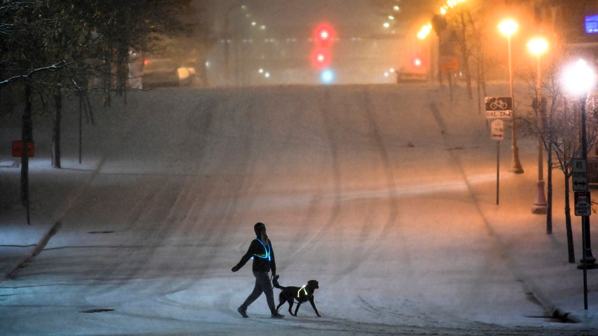 A dog walker crosses a street during Tuesday night's snow storm in downtown Minneapolis, Nov. 10, 2020. (Aaron Lavinsky/Star Tribune via AP)