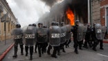 Riot police form a cordon as flames shoot out from the Congress building after protesters set a part of the building on fire, in Guatemala City, Saturday, Nov. 21, 2020. Hundreds of protesters were protesting in various parts of the country Saturday against Guatemalan President Alejandro Giammattei and members of Congress for the approval of the 2021 budget that reduced funds for education, health and the fight for human rights. (AP Photo/Oliver De Ros)