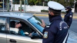 A policeman, wearing a face mask to protect against coronavirus, asks a passenger of a car to display his movement permission form, during the first day of a lockdown, in Athens, Saturday, Nov. 7, 2020. With a surge in coronavirus cases straining health systems in many European countries, Greece has announced a three-week nationwide lockdown. (AP Photo/Yorgos Karahalis)