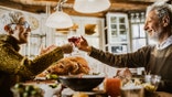 Happy mature couple toasting with wine while having Thanksgiving meal in dining room.