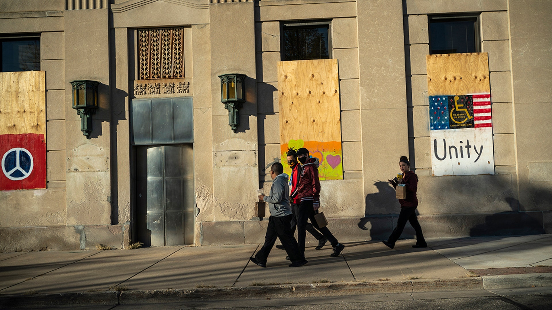 People walk past a bank that has its windows boarded up with plywood in Kenosha, Wis., Saturday, Oct. 31, 2020. Two months after street violence shook the little lakeside city of Kenosha, dozens of businesses are still boarded. Many of these businesses are open, but with divisive elections just days away, some are also hedging their bets, covering up windows and sometimes building outer sets of plywood doors that can be easily shut, like castles pulling up their drawbridges, if trouble returns. (AP Photo/Wong Maye-E)