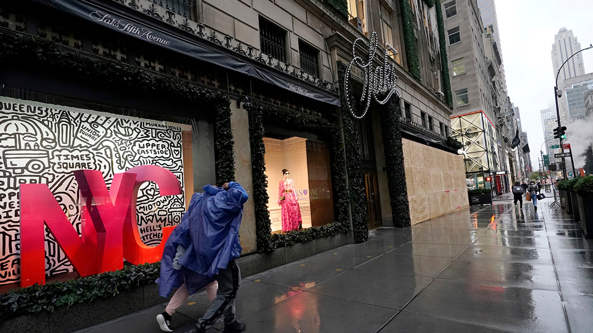 Pedestrians walk past the partially boarded-up windows at Saks Fifth Avenue's flagship Fifth Avenue store, Sunday, Nov. 1, 2020, in New York. Retailers including Nordstrom, Tiffany, and Saks are planning to board up their windows or add extra security personnel in some of their locations ahead of the contentious presidential election on Tuesday.  (AP Photo/Kathy Willens)