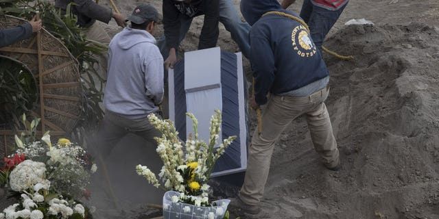 Workers place the coffin of 86-year-old Gabina Salgado Husca, who died of complications related to the new coronavirus, into her grave in the Valle de Chalco municipal cemetery on the outskirts of Mexico City, Wednesday, Nov. 18, 2020. (AP Photo/Marco Ugarte)