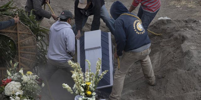Workers place the coffin of 86-year-old Gabina Salgado Husca, who died of complications related to the new coronavirus, into her grave in the Valle de Chalco municipal cemetery on the outskirts of Mexico City, Wednesday, Nov. 18, 2020. (AP Photo/Marco Ugarte)