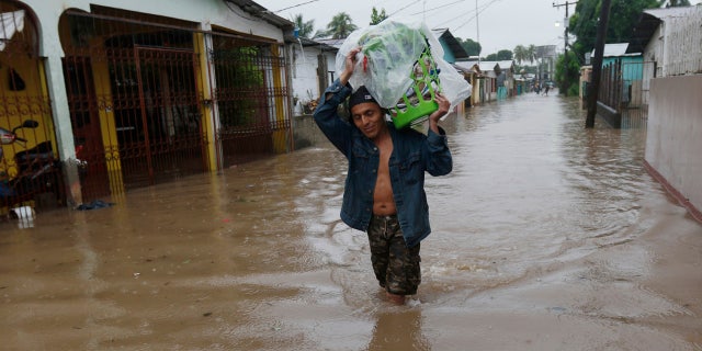 A man walks in knee-deep floodwaters carrying belongings in San Manuel, Honduras, Wednesday, Nov. 4, 2020.