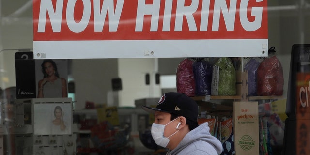 This May 7, 2020, file photo shows a man wearing a mask while walking under a Now Hiring sign at a CVS Pharmacy during the coronavirus outbreak in San Francisco. (AP Photo/Jeff Chiu)