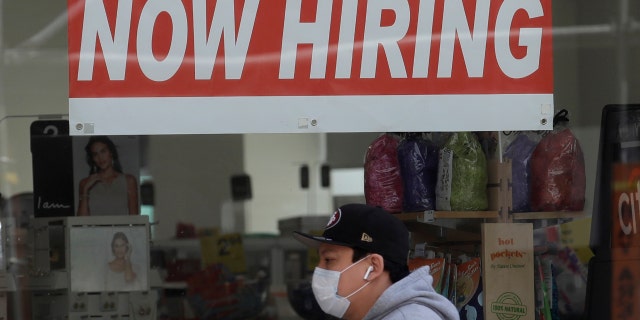 This May 7, 2020, file photo shows a man wearing a mask while walking under a Now Hiring sign at a CVS Pharmacy during the coronavirus outbreak in San Francisco. (AP Photo/Jeff Chiu)