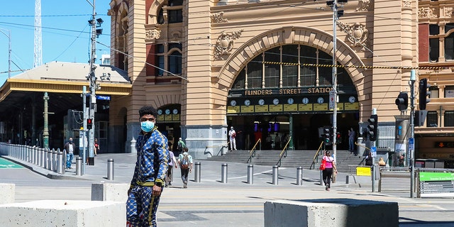 A man wearing a mask walks past Flinders Street Station in Melbourne, Australia, Wednesday, Oct. 28, 2020. In Melbourne, Australia's former coronavirus hotspot, restaurants, cafes and bars were allowed to open and outdoor contact sports can resume Wednesday, emerging from a lockdown due to the coronavirus outbreak. (AP Photo/Asanka Brendon Ratnayake)