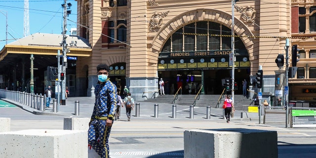 A man wearing a mask walks past Flinders Street Station in Melbourne, Australia, Wednesday, Oct. 28, 2020. In Melbourne, Australia's former coronavirus hotspot, restaurants, cafes and bars were allowed to open and outdoor contact sports can resume Wednesday, emerging from a lockdown due to the coronavirus outbreak. (AP Photo/Asanka Brendon Ratnayake)