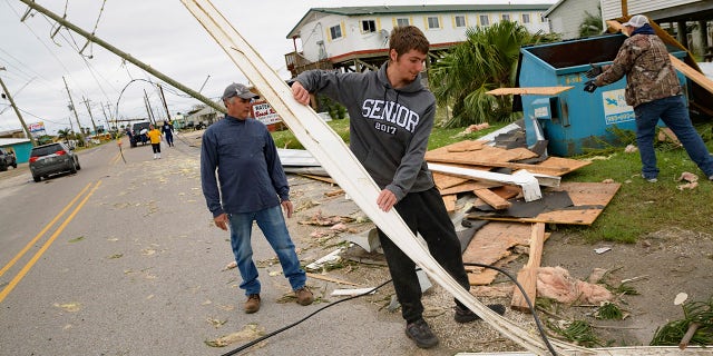 Mark Andollina, left, and his son, Nicholas Andollina, center, remove part of a roof damaged by Hurricane Zeta at the Cajun Tide Beach Resort in Grand Isle, La., Friday, Oct. 30, 2020. (AP Photo/Matthew Hinton)