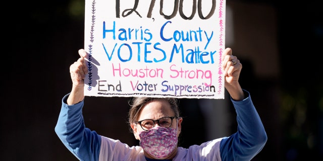 Demonstrator Gina Dusterhoft holds up a sign as she walks to join others standing across the street from the federal courthouse in Houston, Monday, Nov. 2, 2020, before a hearing in federal court involving drive-thru ballots cast in Harris County. (AP Photo/David J. Phillip)