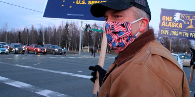 U.S. Sen. Dan Sullivan, an Alaska Republican seeking reelection, waves a sign at a busy intersection Monday, Nov. 2, 2020, in Anchorage, Alaska. Sullivan in the Nov. 3, 2020, election faces Dr. Al Gross, an independent who won the Alaska Democratic primary. (AP Photo/Mark Thiessen)